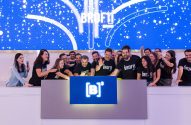 Equipe animada celebra em evento com tela azul festiva e logo [B]* no balcão.