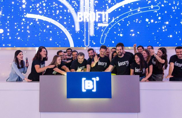 Equipe animada celebra em evento com tela azul festiva e logo [B]* no balcão.