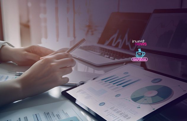 Mãos analisam gráficos e dados em documentos sobre uma mesa, com laptops ao fundo. Ambiente de negócios e planejamento.