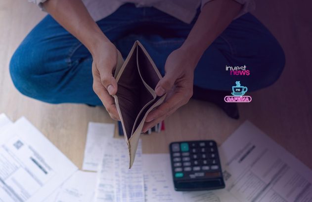 Pessoa sentada no chão segurando carteira vazia, com contas e calculadora espalhadas ao redor.