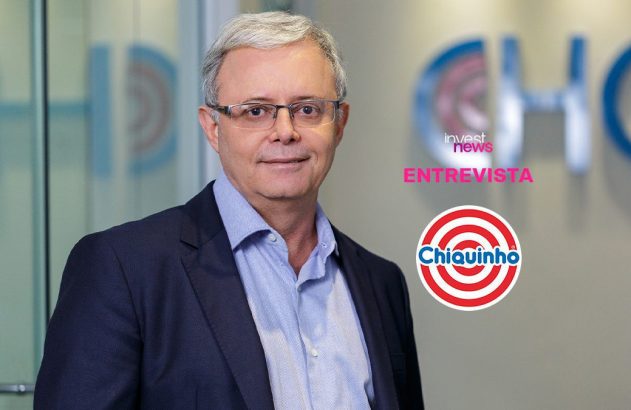 Executivo sorridente em entrevista. Em destaque, logos "Invest News" e "Chiquinho", com fundo de escritório.