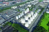 Vista aérea de complexo logístico industrial, com grandes tanques brancos, caminhões e contêineres.