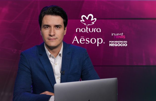 Homem de terno sentado à mesa com laptop, olhando para câmera. Fundo roxo de estúdio com logos.