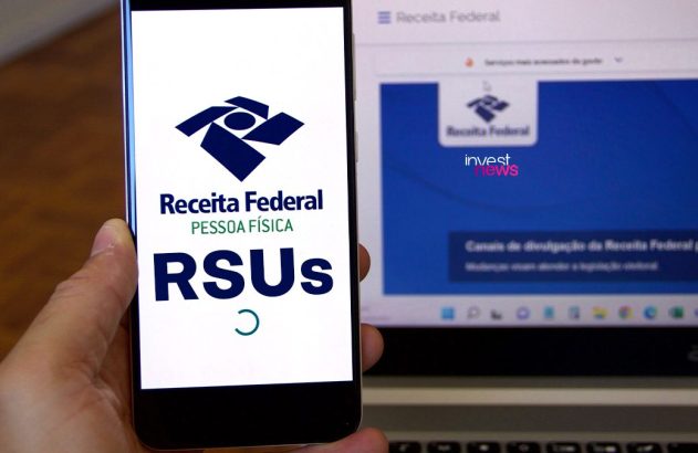Mão segura celular com app Receita Federal RSUs. Notebook mostra portal da Receita Federal ao fundo.