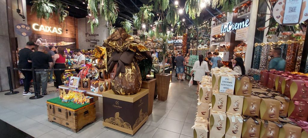 Interior de loja Cacau Show/La Creme, movimentada, com clientes e ovos de Páscoa em destaque.