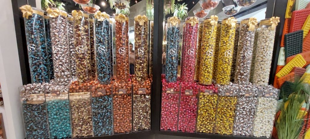 Exibição colorida de chocolates em tubos e caixas transparentes com o logo 'S' e laços dourados.