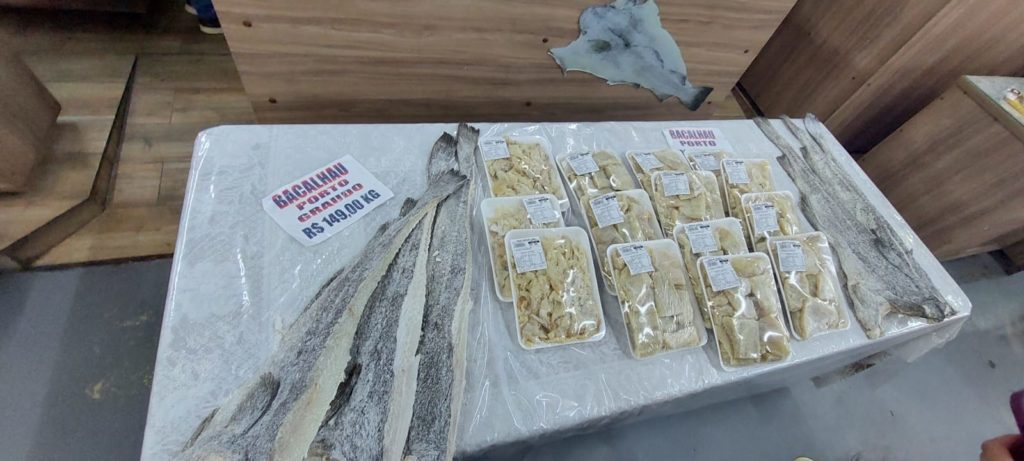 Mesa com bacalhau seco à venda: peças inteiras e embaladas em bandejas. Preço R$ 149,00/kg.