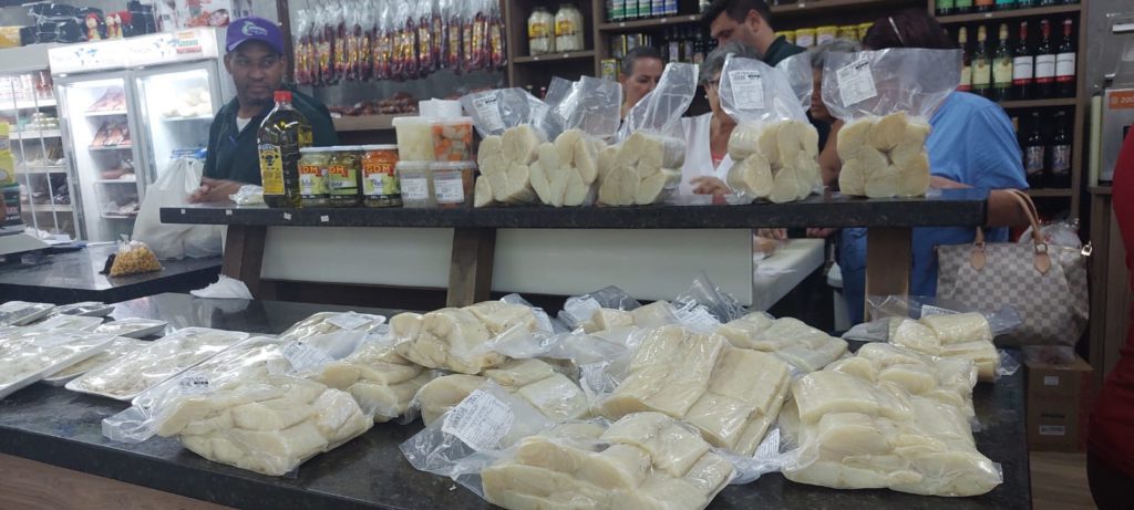 Interior de mercearia com balcões cheios de produtos embalados e pessoas comprando.