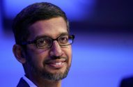 Sundar Pichai sorrindo, de óculos e barba, em fundo azul desfocado.