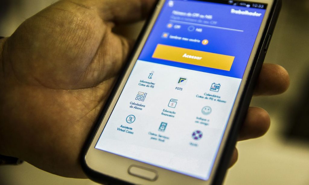Mão segurando um smartphone com o aplicativo "Trabalhador" aberto, mostrando opções como FGTS e PIS.