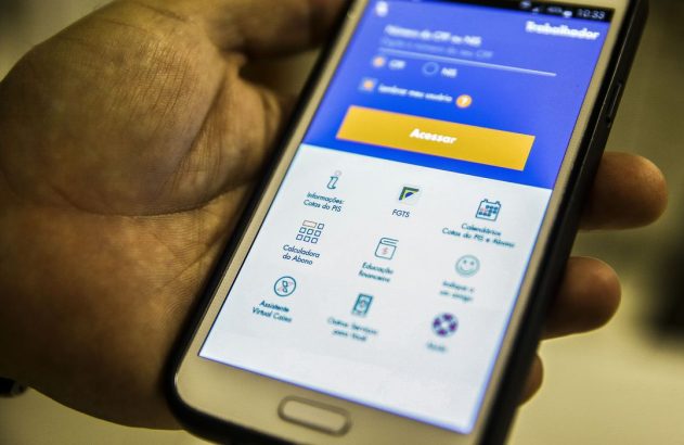 Mão segurando um smartphone com o aplicativo "Trabalhador" aberto, mostrando opções como FGTS e PIS.