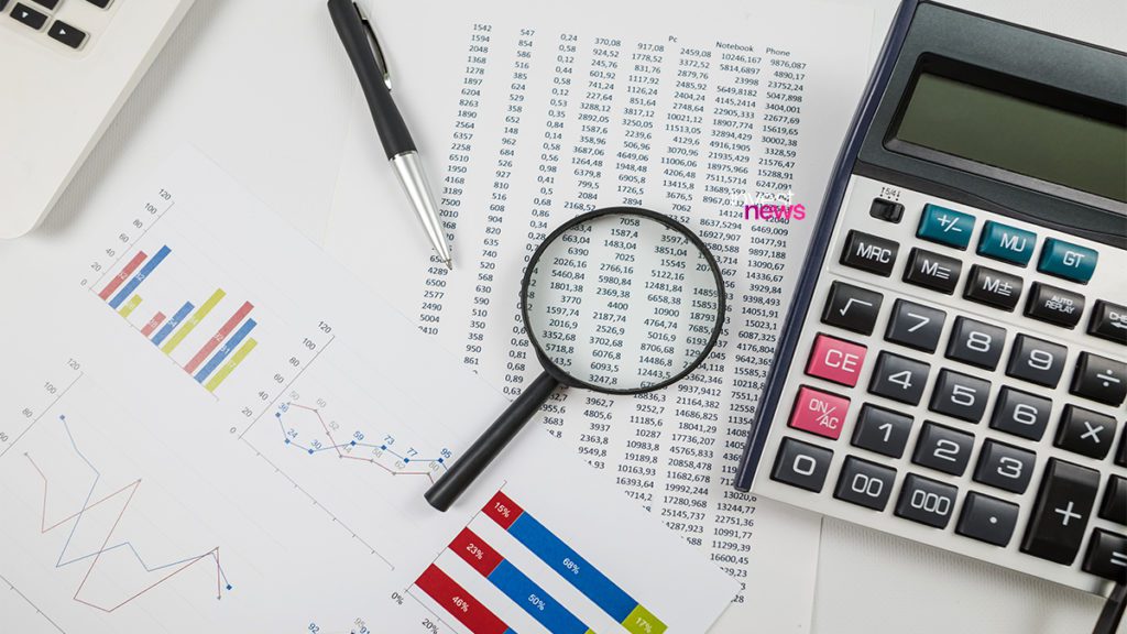 Mesa de escritório com documentos financeiros, calculadora, lupa e caneta, usada para análise de dados e contabilidade.