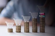 Pilhas de moedas crescentes com carrinhos de compra acima. Uma mão adiciona um carrinho à maior pilha.