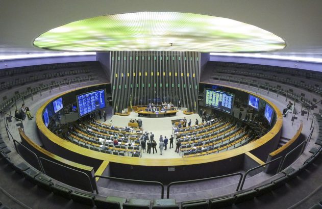 Plenário do Congresso, com parlamentares em sessão e telas exibindo dados. Teto iluminado.