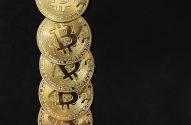 Moedas douradas de Bitcoin empilhadas verticalmente em fundo preto.