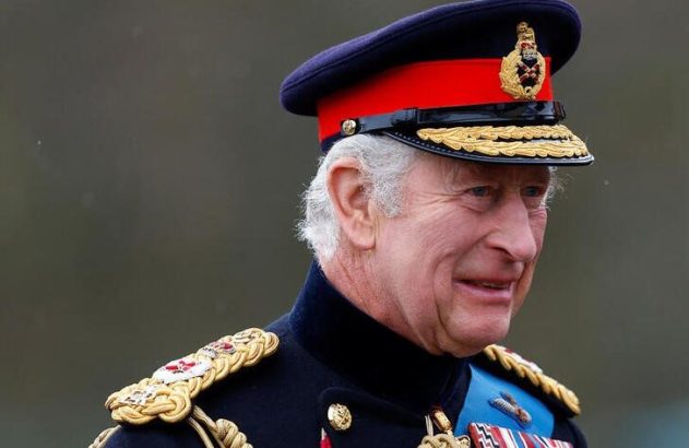 Rei Charles III, em uniforme de gala militar azul-marinho com chapéu e medalhas, olhando à direita.