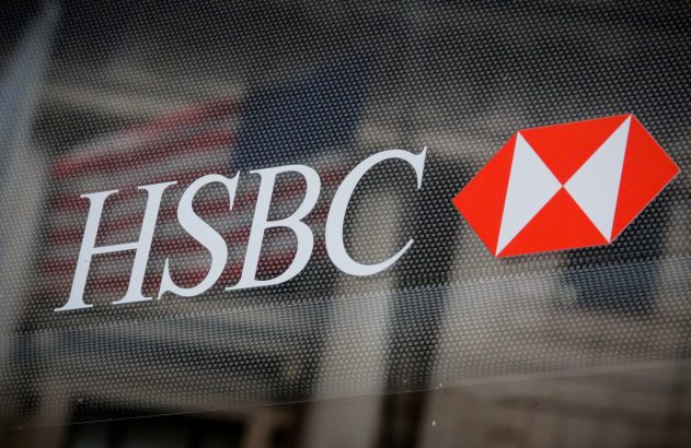Logotipo do HSBC em branco e vermelho em um vidro pontilhado, com reflexo de bandeira ao fundo.
