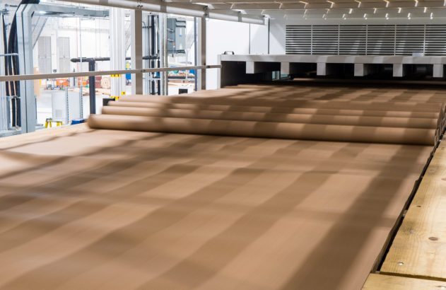 Carpete marrom sendo desenrolado em linha de produção industrial.