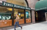 Homem caminha na calçada em frente ao First Republic Bank, com letreiros e fachada visíveis.