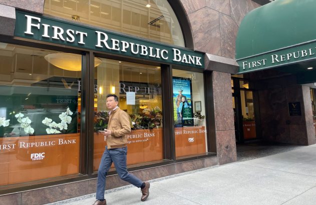 Homem caminha na calçada em frente ao First Republic Bank, com letreiros e fachada visíveis.