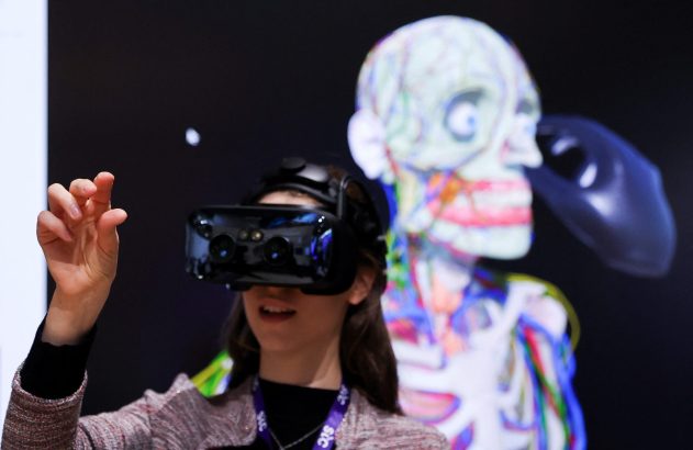 Jovem com óculos VR e mão levantada interage com um modelo 3D de esqueleto em tela.