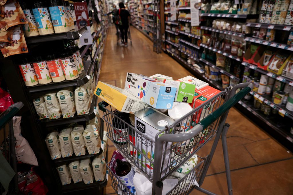 Carrinho de compras cheio de produtos 365 Whole Foods Market em corredor de supermercado.