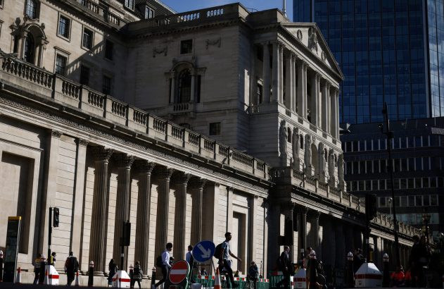 Vista externa de um edifício clássico com colunas e pessoas andando na calçada. Arranha-céu moderno no fundo.
