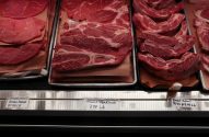 Cortes de carne (bifes, costelas) em vitrine de açougue com etiquetas de preço visíveis.