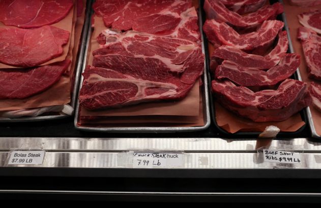 Cortes de carne (bifes, costelas) em vitrine de açougue com etiquetas de preço visíveis.
