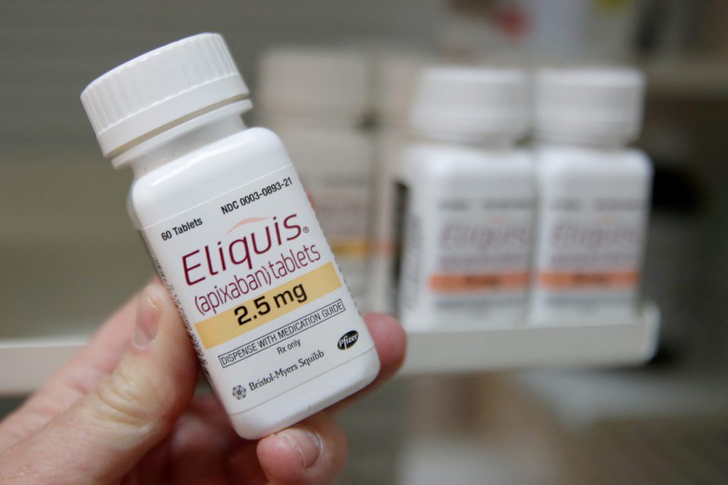 Mão segurando frasco de Eliquis (apixaban) 2.5 mg.
