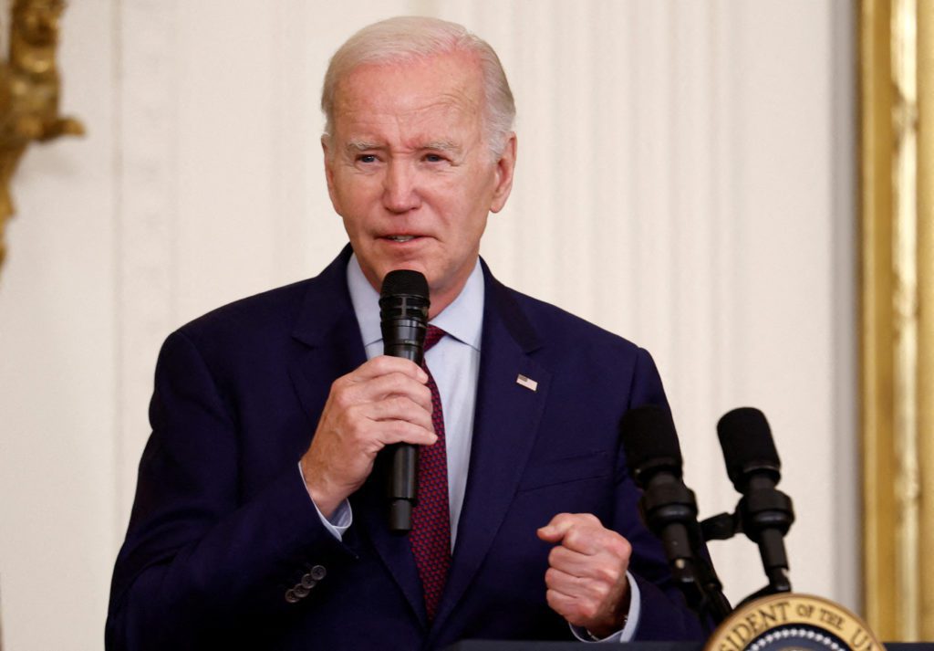 Joe Biden, de terno, segurando um microfone e falando.