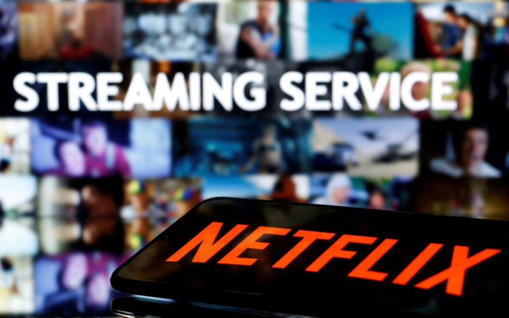 Smartphone com logo Netflix. No fundo, tela com 'Streaming Service' e vídeos borrados.