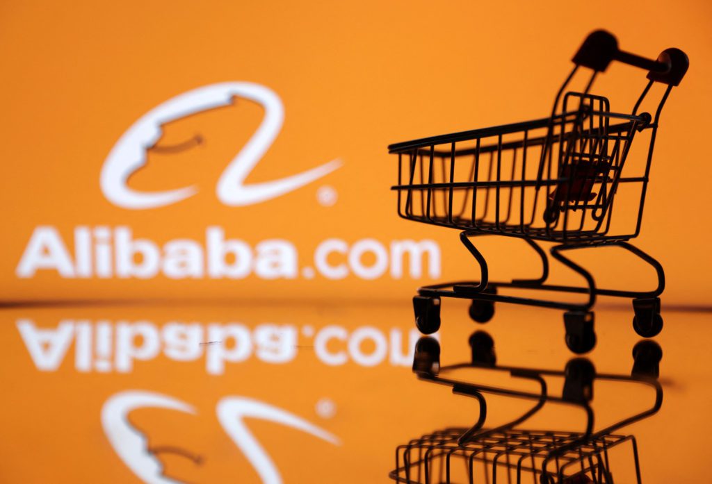 Carrinho de compras miniatura com logo Alibaba.com em fundo laranja reflexivo.