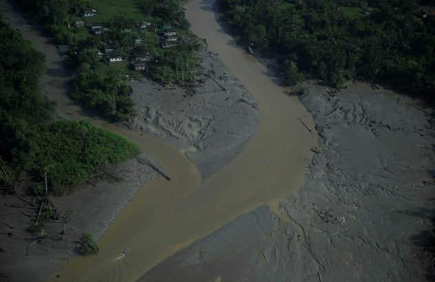 Vista aérea de rio barrento e vastas margens de lama. Há um vilarejo com casas entre a vegetação e a água.