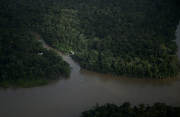 Confluência de rios marrons em floresta densa, com casas e barcos às margens.