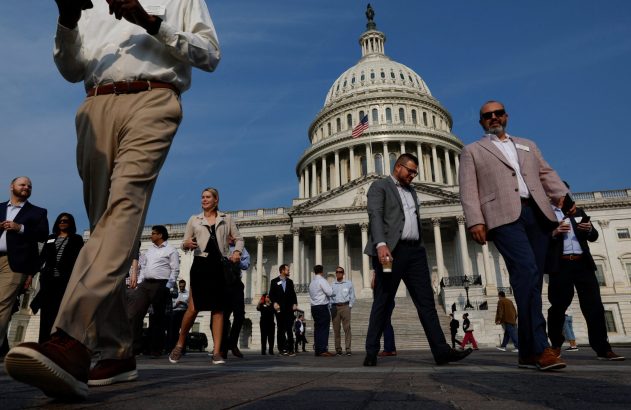 Vista baixa de pessoas caminhando em frente ao Capitólio dos EUA. Homem em cáqui no primeiro plano.