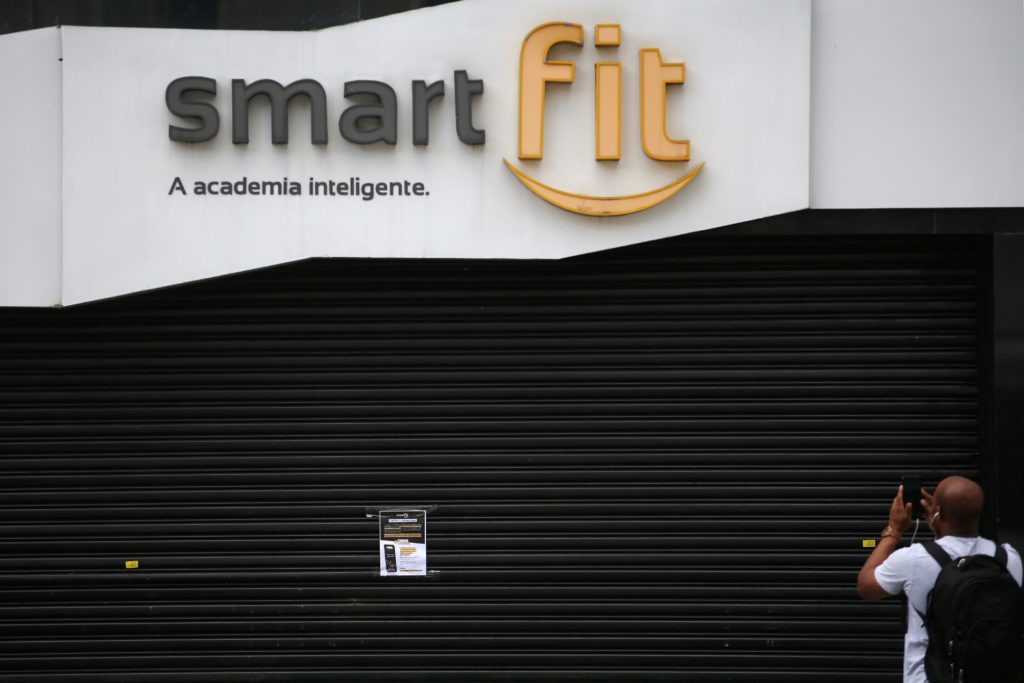 Fachada da Smart Fit fechada por porta de enrolar, com homem fotografando.