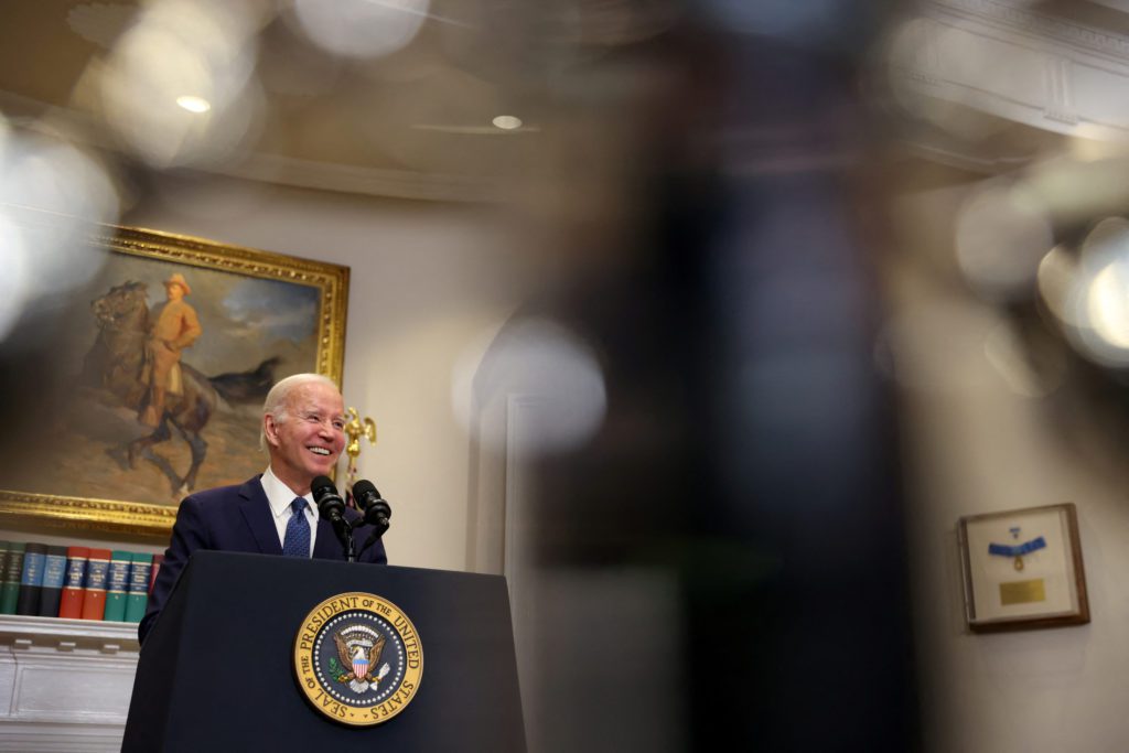 Joe Biden sorri enquanto fala em um pódio com o selo presidencial dos EUA.