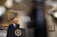 Joe Biden sorri enquanto fala em um pódio com o selo presidencial dos EUA.