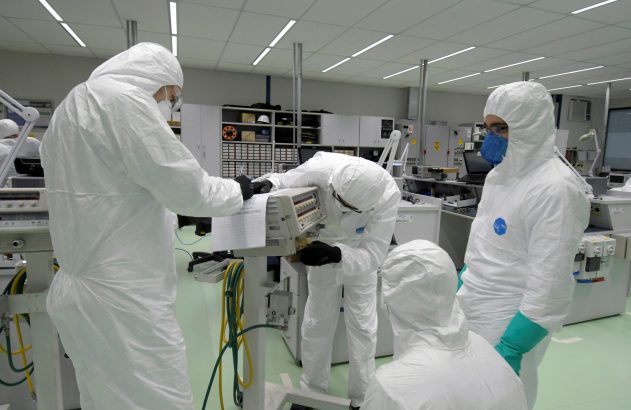Equipe em macacões brancos de proteção trabalha com equipamentos em um laboratório.