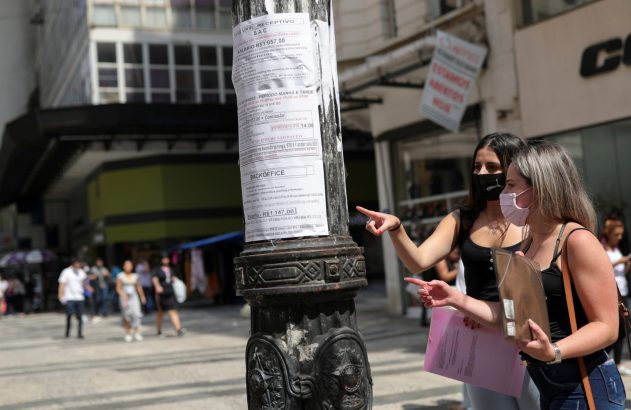 Duas mulheres com máscaras observam anúncios de emprego em um poste, uma delas aponta.