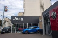 Concessionária de carros com marcas Jeep, Alfa Romeo, Fiat e Abarth. Um Jeep preto e um SUV azul estacionados.