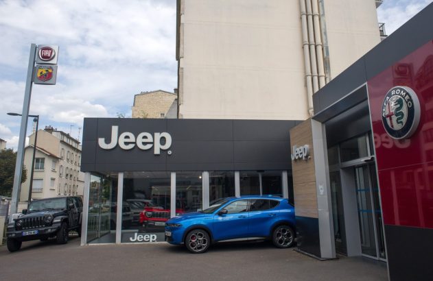 Concessionária de carros com marcas Jeep, Alfa Romeo, Fiat e Abarth. Um Jeep preto e um SUV azul estacionados.