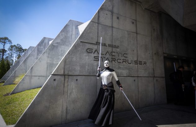 Inquisidor com sabres de luz posando em frente ao edifício Star Wars Galactic Starcruiser.