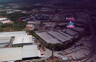 Vista aérea de complexo industrial com galpões. Logo "Invest News" com xícara de café sobreposto digitalmente.