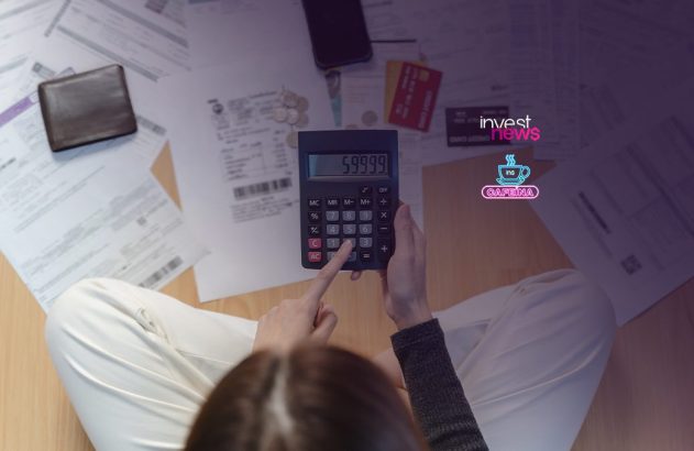 Pessoa sentada no chão usando calculadora para organizar contas, cercada por papéis, carteira e cartões.