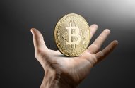Mão segurando uma moeda dourada de Bitcoin.