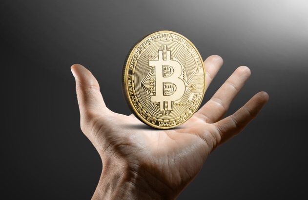 Mão segurando uma moeda dourada de Bitcoin.
