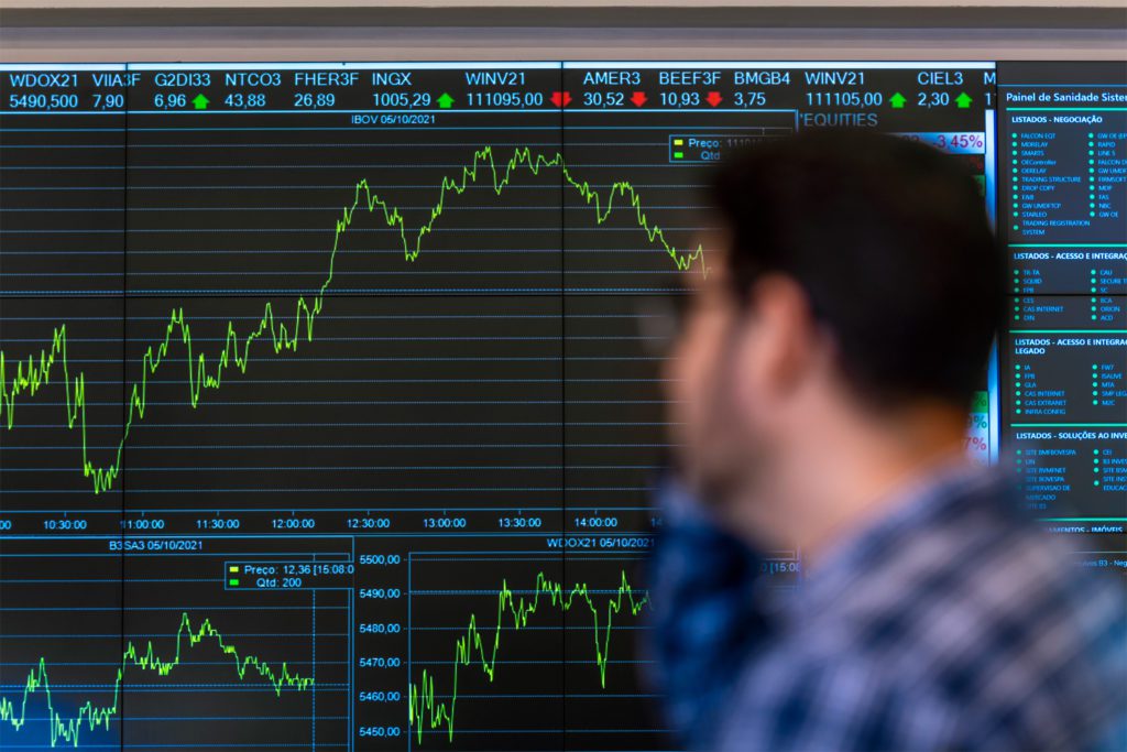 Pessoa observa monitor exibindo gráficos e dados do mercado de ações.