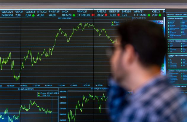 Pessoa observa monitor exibindo gráficos e dados do mercado de ações.